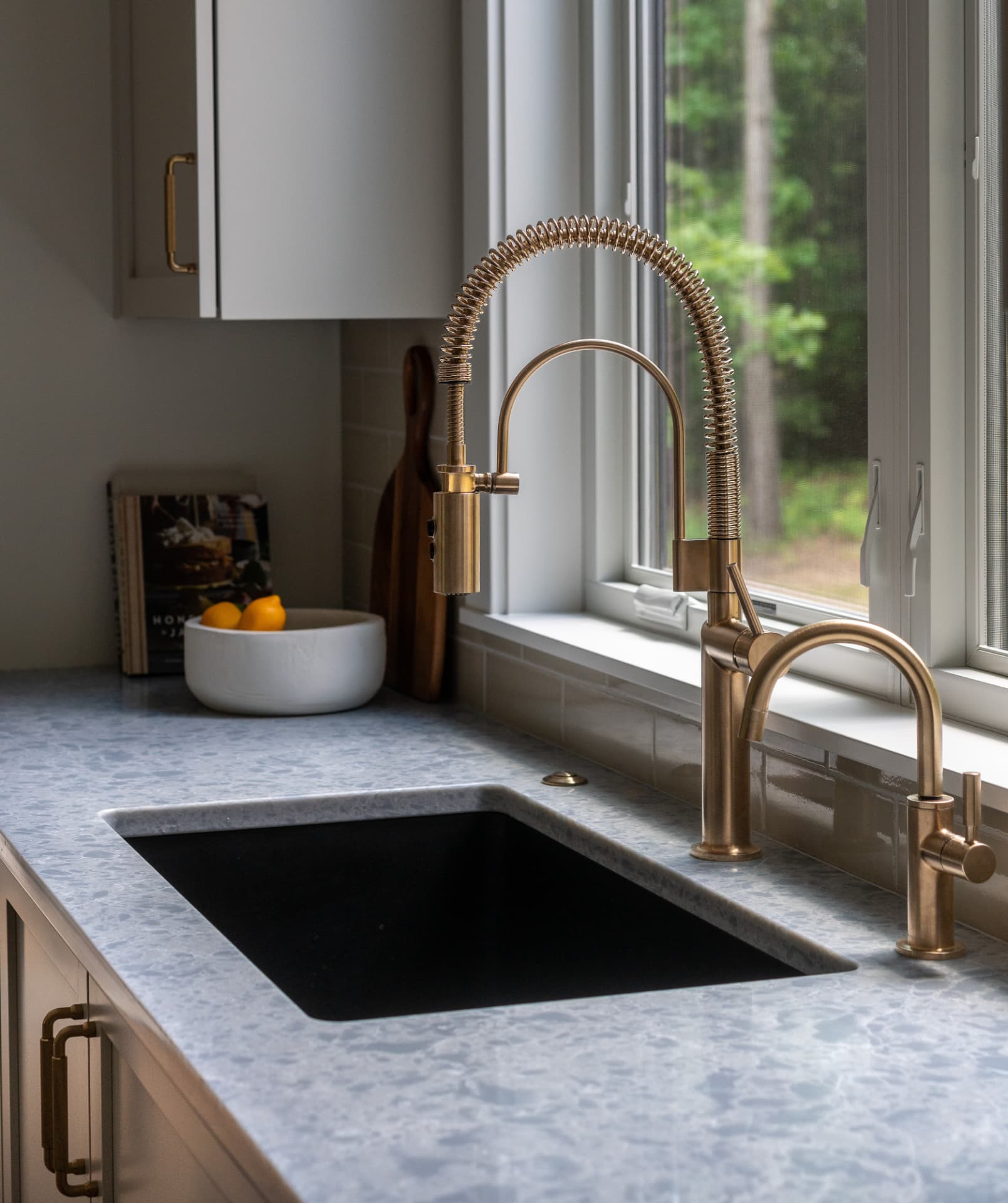 Kitchen detail with brass faucet and honed stone countertop by a window