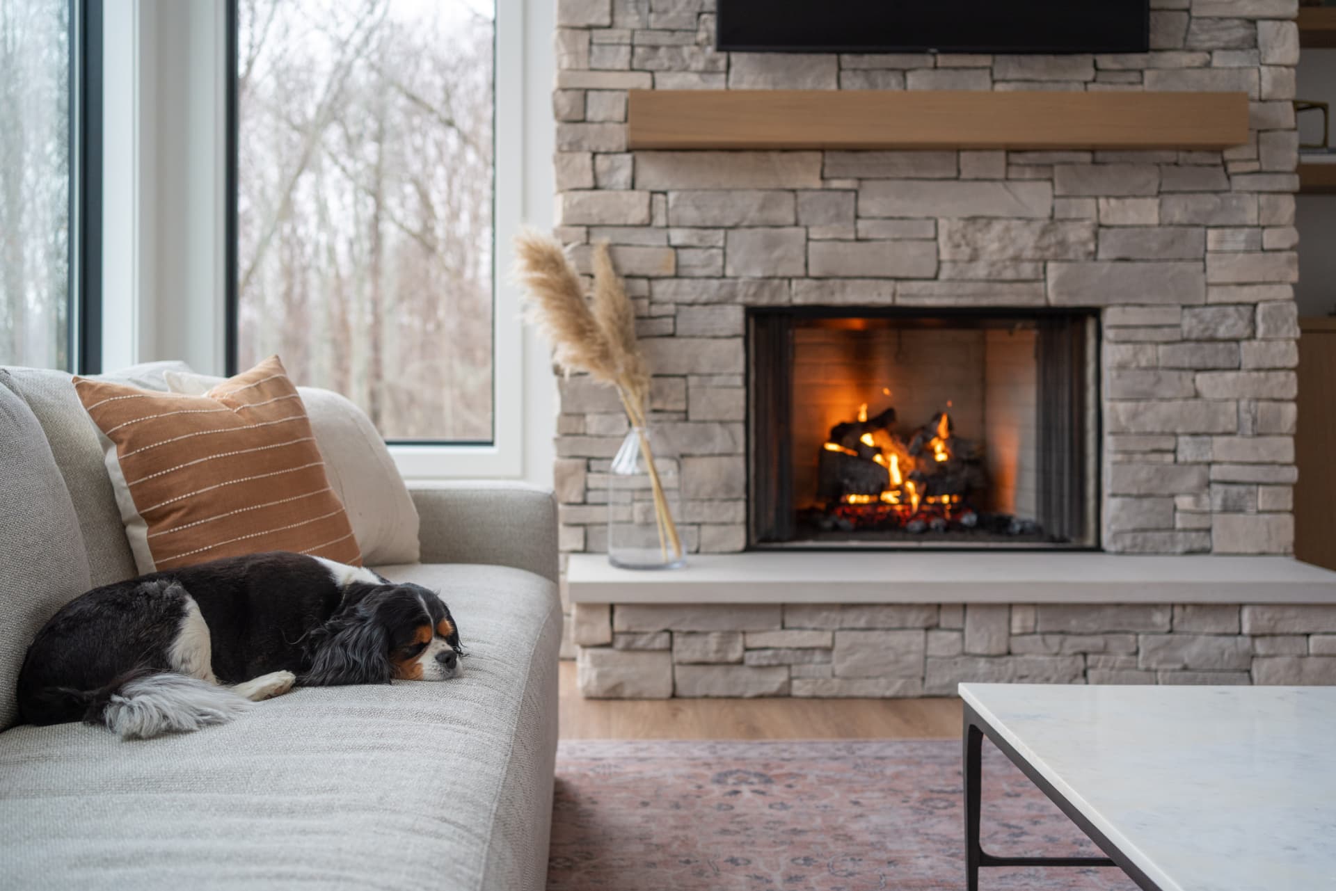 Stone fireplace with oak mantel, linen sofa and a dog resting in the light
